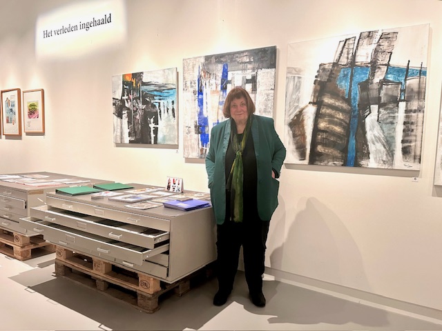 Kunstenaar staat tussen de schilderijen van de expositie Het verleden ingehaald.